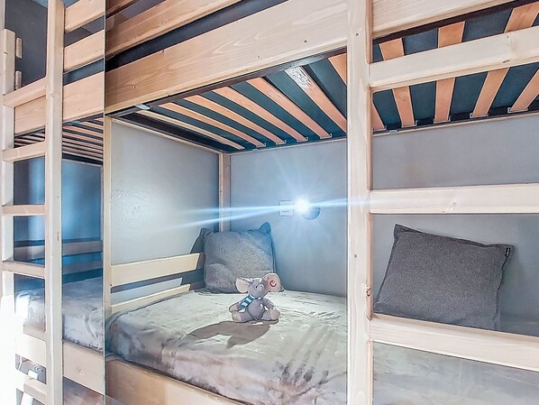 A bunk bed room with a sloped ceiling, a small window, and a teddy bear on the lower bunk.