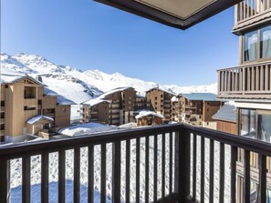 Un paysage montagneux enneigé, avec en arrière-plan un immeuble à plusieurs étages doté de balcons, qui semble être un hôtel ou un complexe touristique.