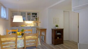Une cuisine compacte avec des meubles blancs, un luminaire suspendu et un petit coin repas comprenant une table et des chaises.