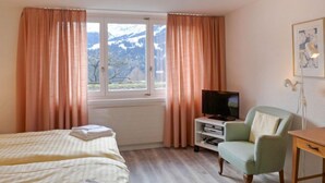 Une chambre d’hôtel avec un lit, un téléviseur posé sur un meuble, une chaise et un bureau.