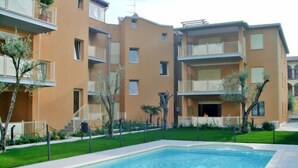 Un moderno edificio de apartamentos con piscina, balcones y un jardín bien cuidado.