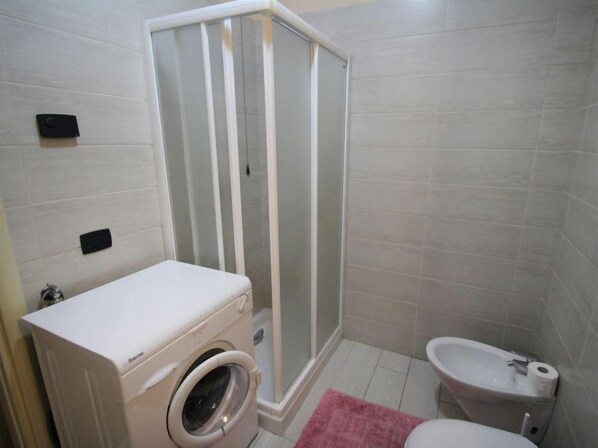 A small bathroom with a washing machine, a shower enclosure, and a sink.