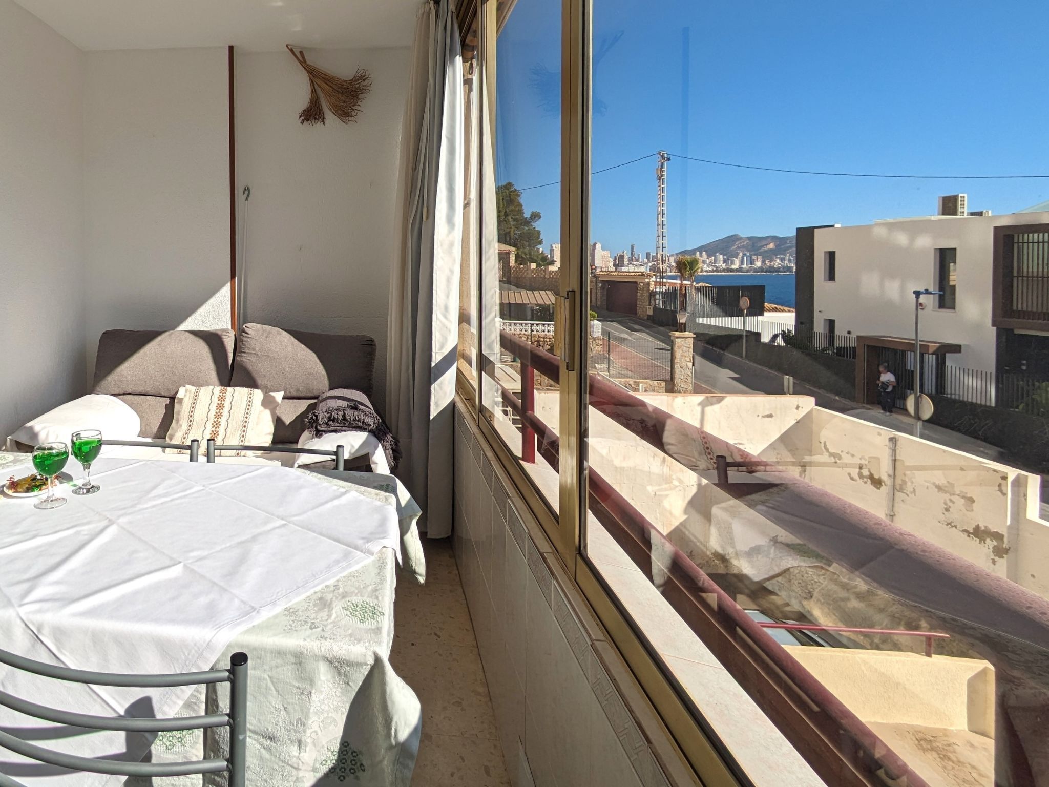 Un balcón con una mesa preparada para dos personas, una cama con almohadas y vistas a la ciudad y a las montañas.
