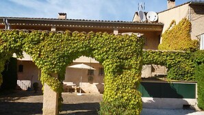Un edificio con un arco de piedra cubierto de hiedra, un patio con mesa y sillas, y antenas parabólicas en el techo.
