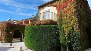 Un edificio con fachada singular cubierta de hiedra y hojas coloridas, un seto cuidado y un cielo despejado.