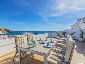 A terrace with a table set for two, overlooking a coastal view.