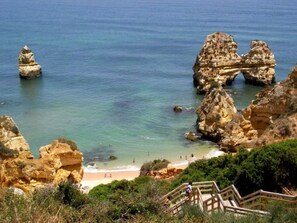 A coastal landscape with rocky formations, clear blue water, and a sandy beach.