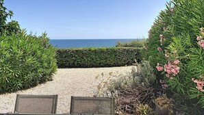 A pathway leading to a beach with a clear view of the sea, surrounded by greenery and a gravel area.