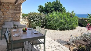 An outdoor dining area with a table set for two, stone walls, and a view of the sea.