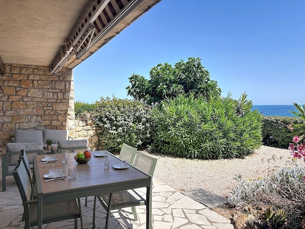 An outdoor dining area with a table set for two, stone walls, and a view of the sea.