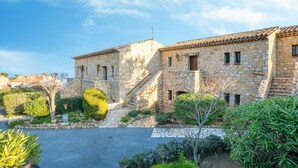 A stone building with a tiled roof, a paved courtyard, and surrounding greenery.