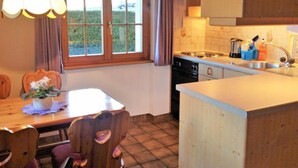 A kitchen with a dining table, chairs, a window with curtains, a sink, and a stove. - Lohnerhus by Interhome (Grindelwald)