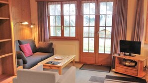 A cozy living room with a sofa, a coffee table, a TV stand, and a bookshelf. - Lohnerhus by Interhome (Grindelwald)