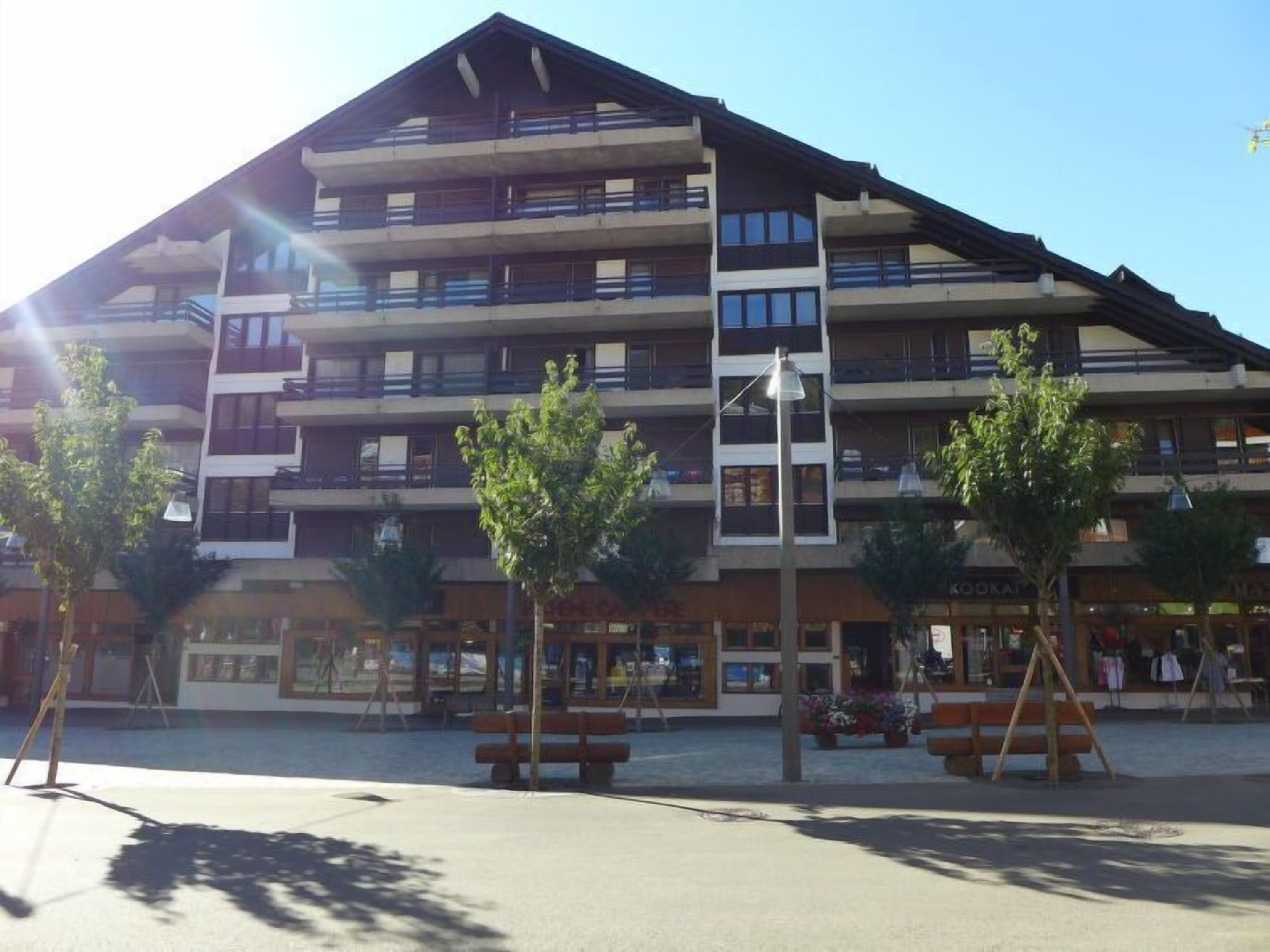 Ein mehrstöckiges Hotel mit Balkonen, einem zentralen Innenhof mit Bänken und wolkenlosem Himmel.
