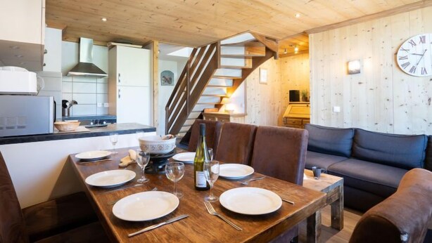 A dining area with a wooden table set for four, a staircase, and a living room with a sofa. - Lac Blanc 704 by Interhome (Val Thorens)