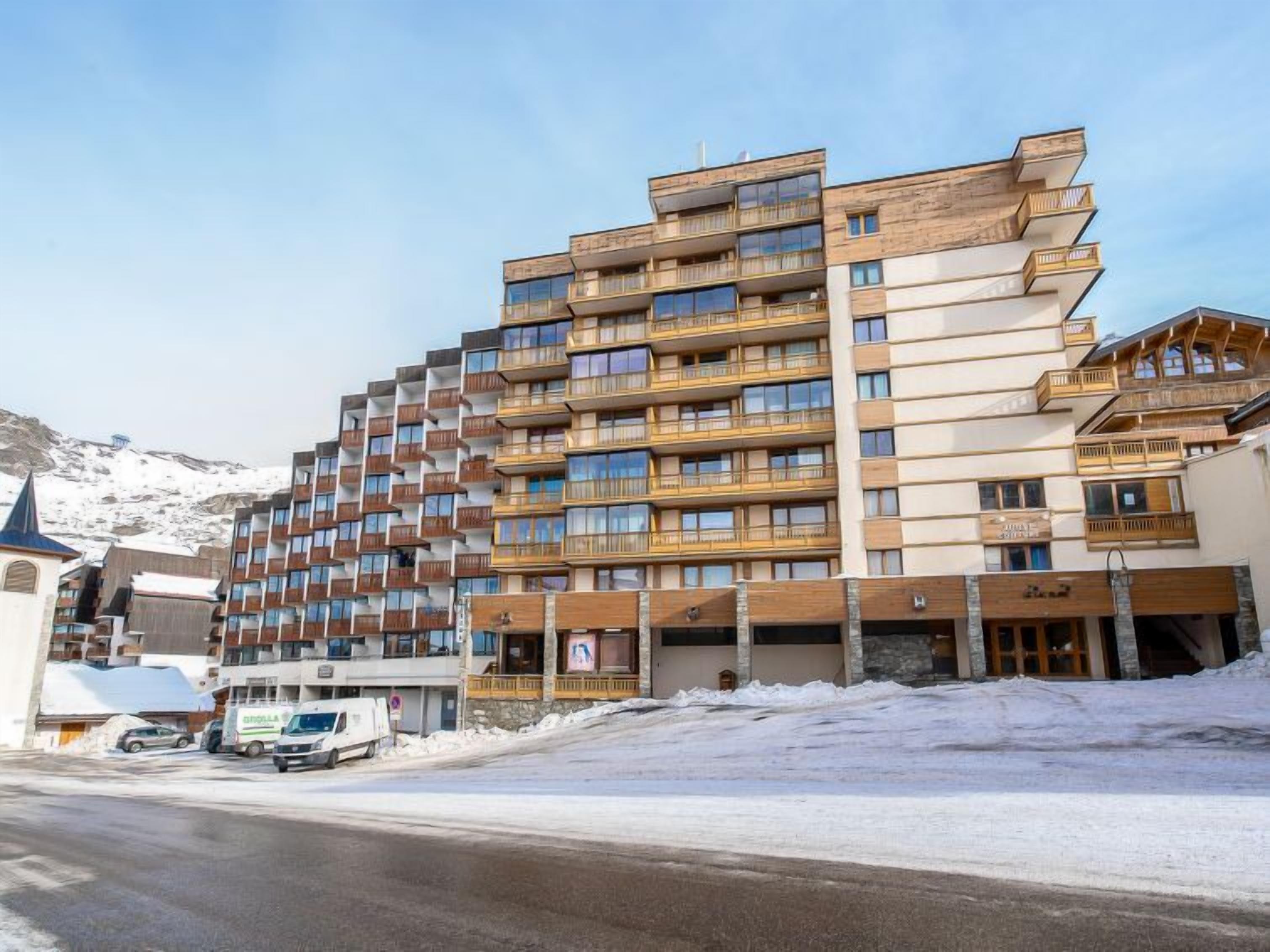 Un hotel a più piani con balconi, una seggiovia sullo sfondo e un paesaggio innevato.