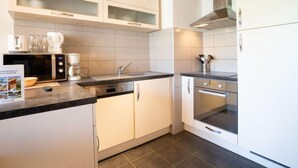 A modern kitchen with white cabinets, a black countertop, and stainless steel appliances including a microwave, coffee maker, and oven. - Lac Blanc 704 by Interhome (Val Thorens)