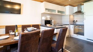 A modern kitchen with white cabinets, a built-in microwave, and a stove. There is a dining area with a wooden table and brown chairs. - Lac Blanc 704 by Interhome (Val Thorens)
