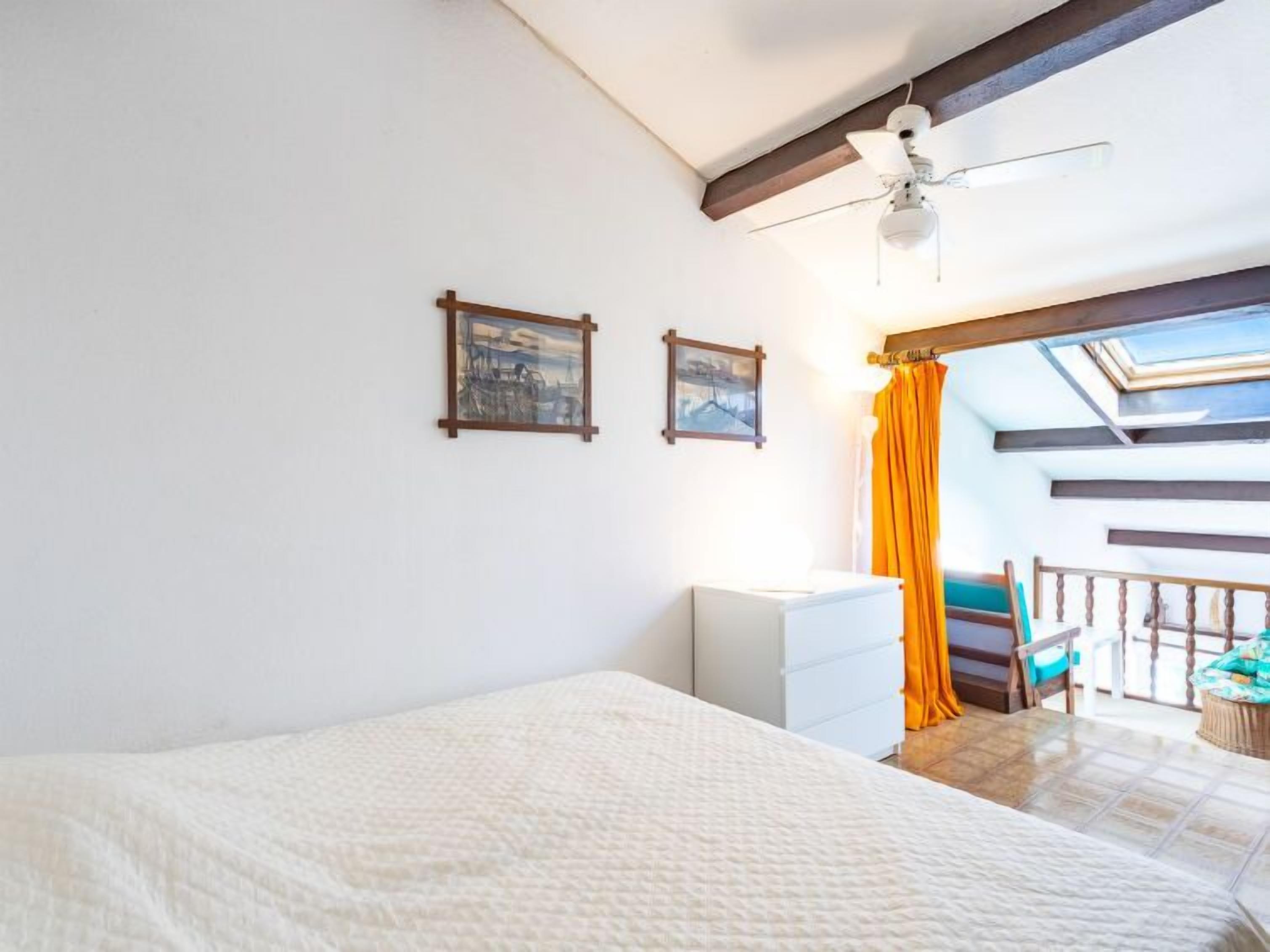 Ein Schlafzimmer mit einem Bett, einem Deckenventilator und einem Fenster mit Vorhängen.
