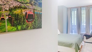 A hotel room with a bed, a window with curtains, and a wall with a large painting of a cable car. - FeWo Sun & Snow by Interhome (Bad Hofgastein)