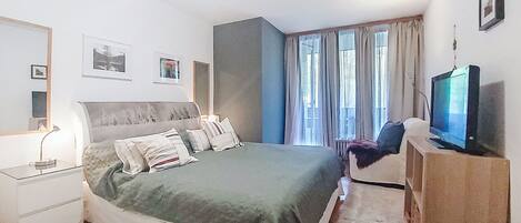 Ein Schlafzimmer mit Bett, Nachttisch, Lampe, Fernseher und Vorhängen.