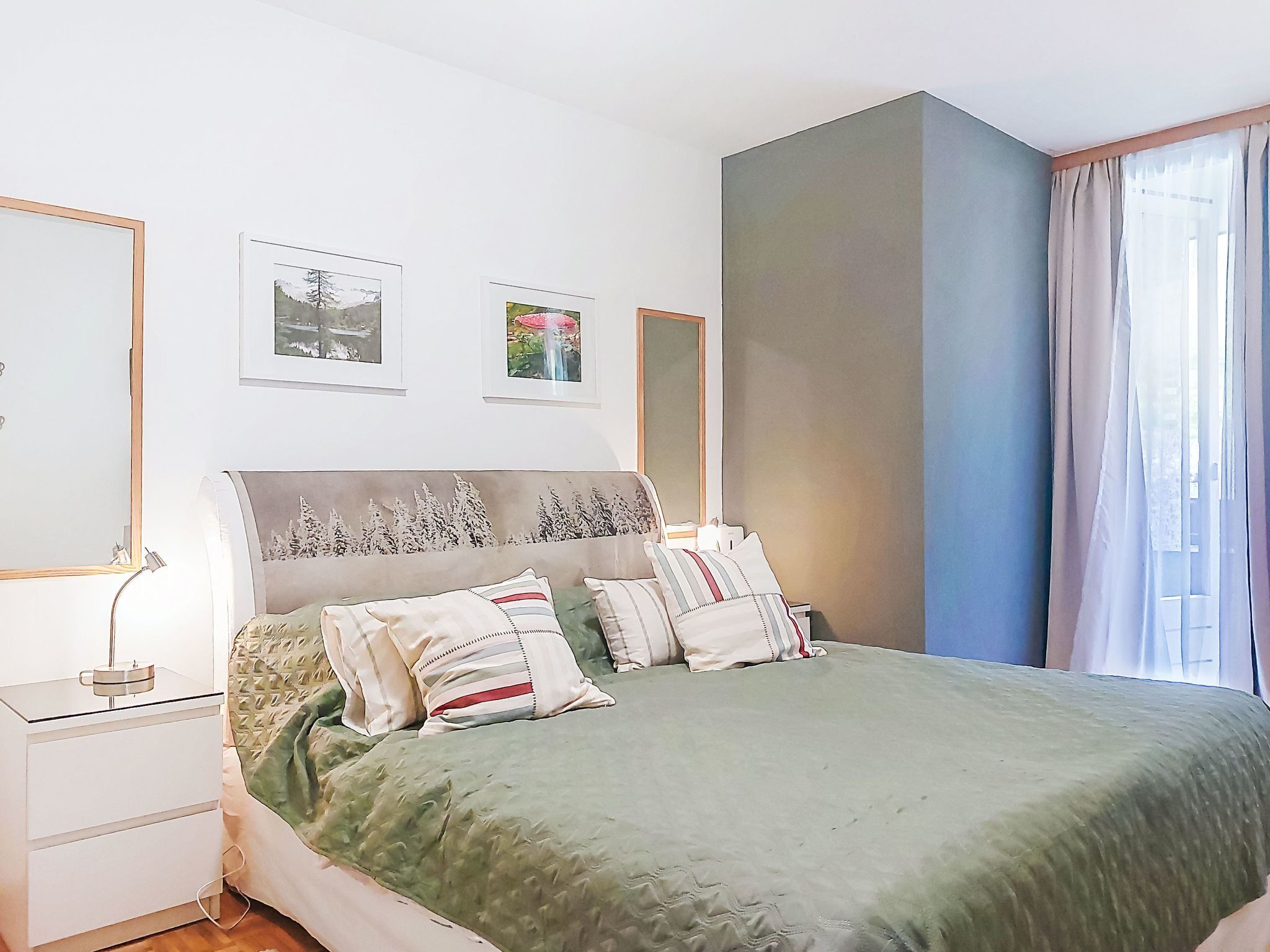 A bedroom with a bed, bedside tables, a nightstand, and wall-mounted pictures.