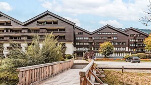 A modern multi-story building with balconies, a wooden bridge, and a parking area. - FeWo Sun & Snow by Interhome (Bad Hofgastein)