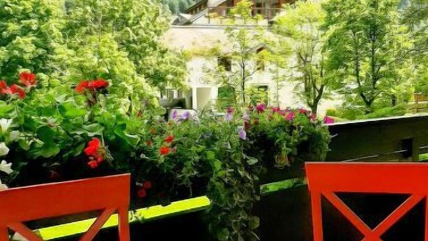 A table with a teapot and cups, surrounded by chairs, overlooking a mountainous landscape with greenery and a house. - FeWo Sun & Snow by Interhome (Bad Hofgastein)