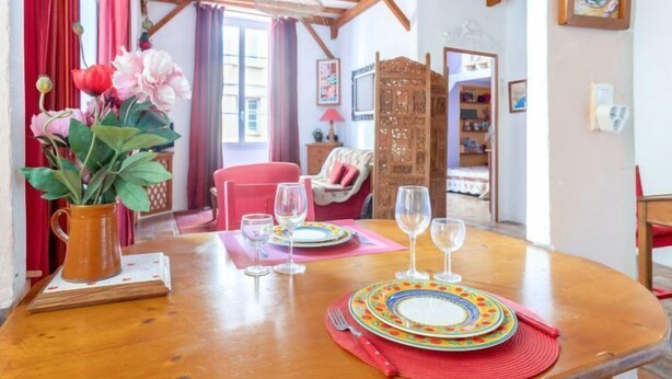 Ein Essbereich mit Holztisch, gedeckt für zwei Personen, einer Blumenvase und Blick in einen Raum mit Bett und einer Holzvertäfelung.