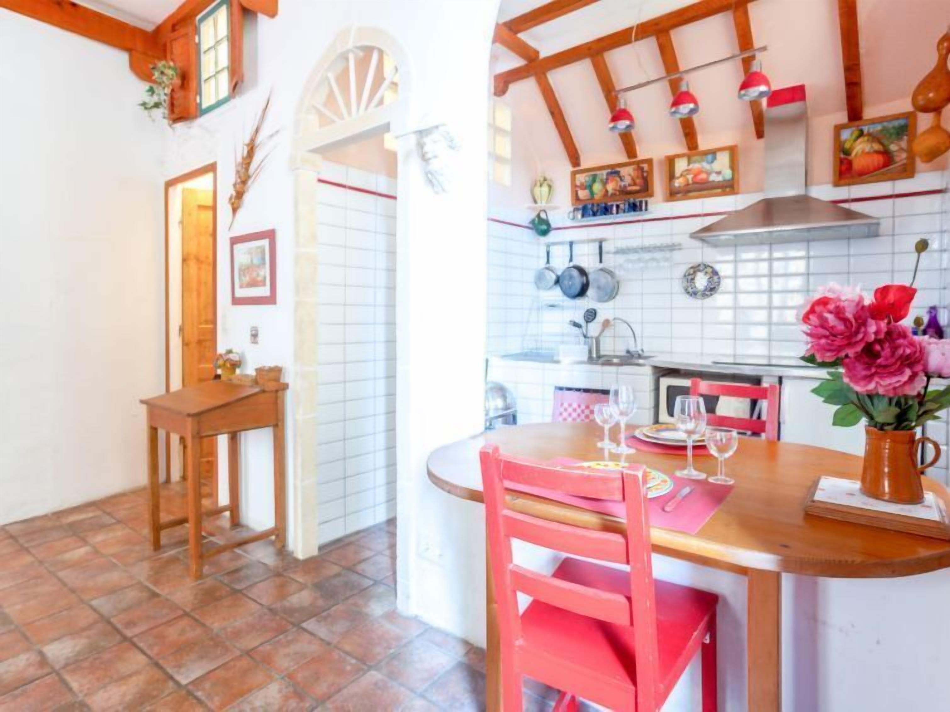 Une cuisine chaleureuse avec des poutres en bois, un dosseret carrelé et un coin repas comprenant une chaise et une table rouges.