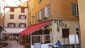 Ein Café namens 'Rene Socca' mit Außenbestuhlung und einer roten Markise.