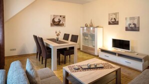 A modern living room with a dining table, chairs, a sofa, a TV stand, and artwork on the walls.