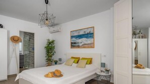 Camera da letto moderna con un letto grande, un quadro che raffigura una spiaggia, una pianta e un'originale lampada geometrica.