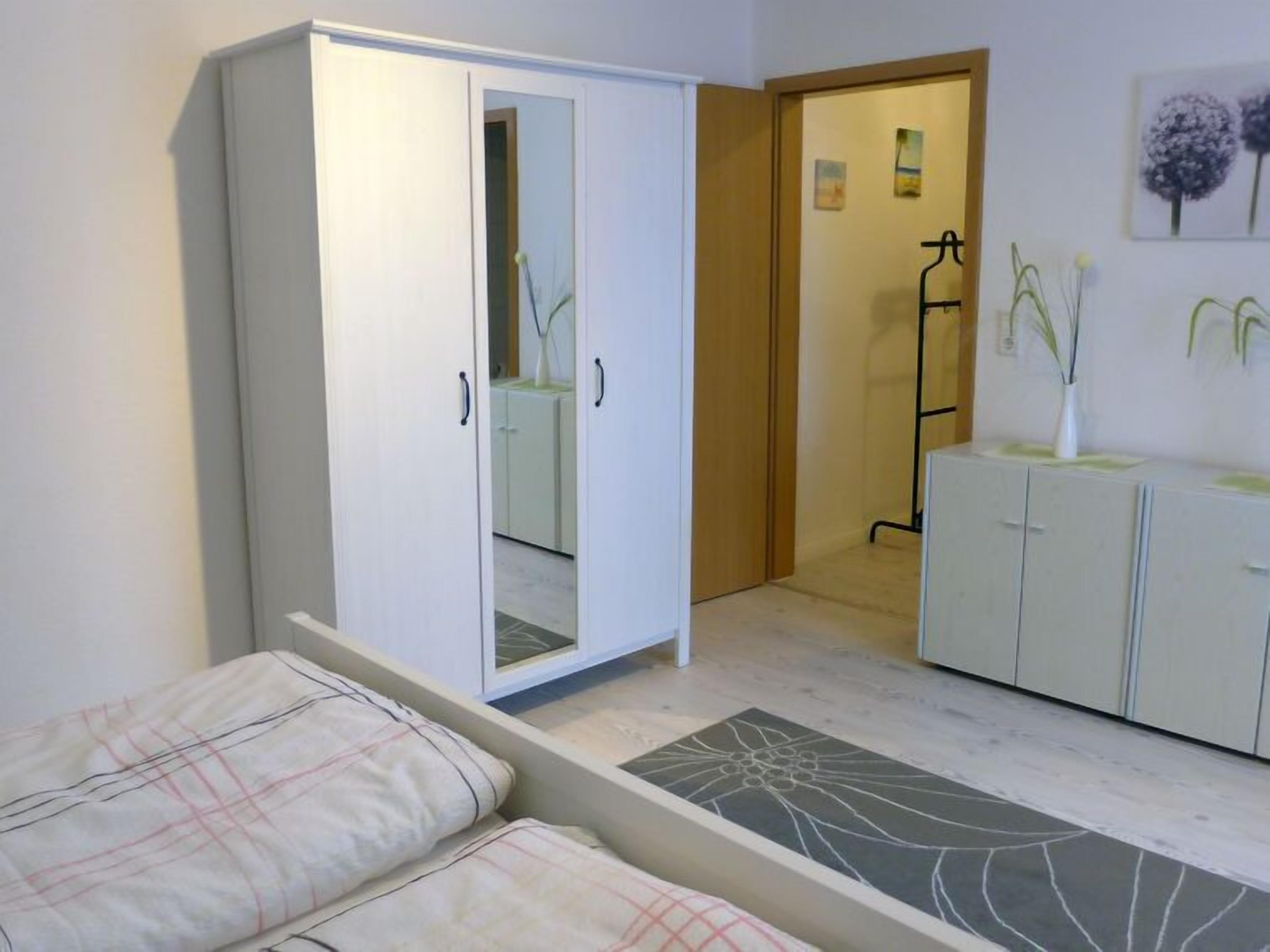 Un dormitorio con armario, cama con ropa de cama estampada, mesita de noche, espejo y un mueble pequeño.