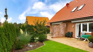 Une maison avec une façade en briques, un toit en tuiles et un jardin bien entretenu, avec une pelouse et diverses plantes.