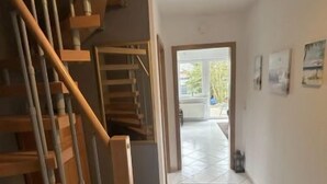 Un escalier menant à un palier où se trouve un tapis noir, une porte donnant sur un espace extérieur et un sol carrelé.