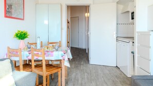 A compact kitchen with white cabinets and a microwave. A dining area with a table set for two and a chair is visible. - les Goelands by Interhome (Mimizan)