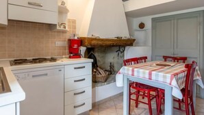 A compact kitchen with a gas stove, a red coffee machine, and a dining table with red chairs. - Canneto by Interhome (Marina di Andora)