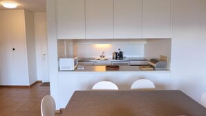 A modern kitchen with white cabinets, a dining table with four chairs, and a small island with a kettle and coffee maker. - Monte Cristo 6 by Interhome (Crans-Montana)