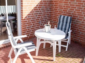 A patio with a white table and two striped chairs, a brick wall, and a glass door. - Westerriede by Interhome (Norddeich)