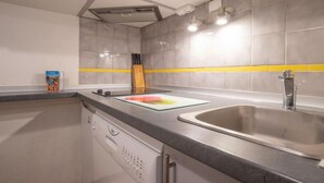 A kitchen with a dishwasher, a sink, and a cutting board on the counter. - Balcons d'Olympie 305 - A by Interhome (Les Menuires)