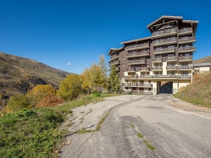 A multi-story hotel with balconies, situated in a hilly area with autumn foliage.