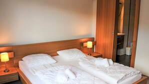 A double bed with a wooden headboard, two bedside tables with lamps, and a mirror on the wall. - Andromède 3-pièces A34 by Interhome (Moléson-sur-Gruyères)