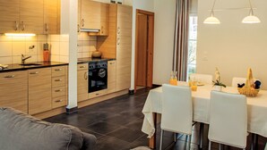 A modern kitchen with wooden cabinets, a built-in oven, and a dining area with a table and chairs. - Andromède 3-pièces A34 by Interhome (Moléson-sur-Gruyères)