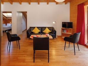 A modern living room with a sofa, two chairs, a coffee table, a TV, and a bookshelf.