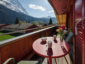 Un balcon avec une table dressée pour deux personnes, un vase rempli de fleurs et une vue sur les montagnes et les maisons.