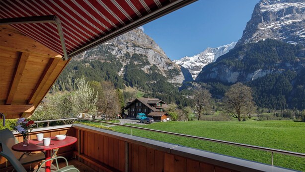 A wooden deck with a table and chairs, overlooking a mountain landscape with a chalet. - Chalet Almisgässli by Interhome (Grindelwald)