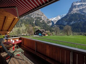 Eine HolzdTerrasse mit Tisch und Stühlen mit Blick auf eine Berglandschaft und eine Chalet.