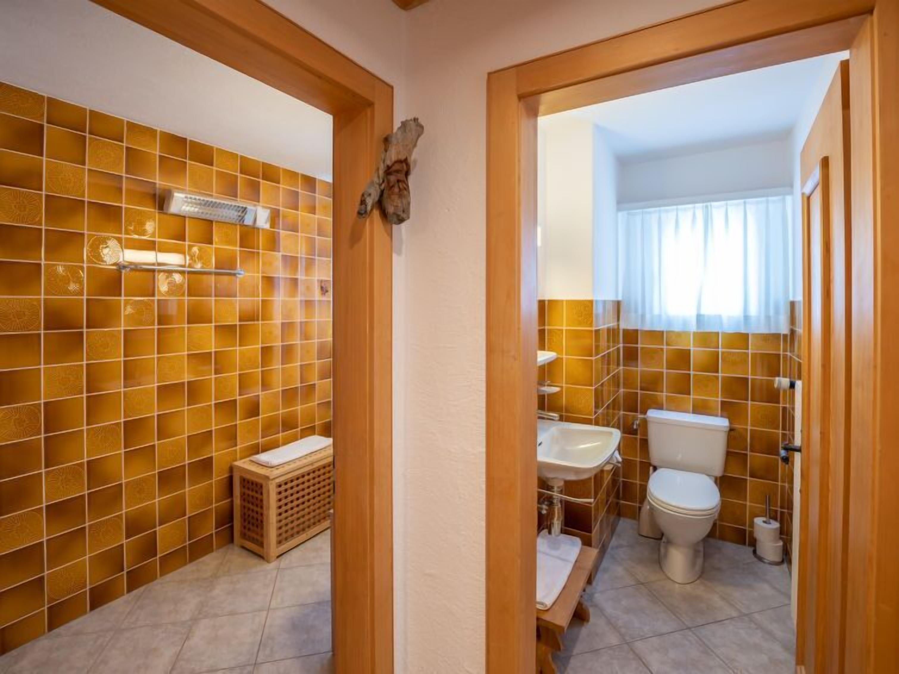Ein Badezimmer mit gefliesten Wänden, einer Holzbank, einer Toilette, einem Waschbecken und einer Duschkabine.