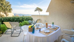 Een terras met een tafel gedekt voor twee personen, omringd door witte stoelen, met uitzicht op zee en een heldere lucht.